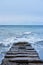 Waves break on rocks and fly apart into small drops and turn into foam. Long concrete breakwater stretching away into depths of