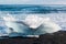 Waves breaking on an iceberg on a black sand beach at Jokulsarlon ice lagoon, Iceland