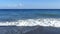 Waves breaking on the shore with sea foam.. Greece, Santorini island. Perissa beach with black volcanic sand