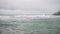 Waves crash against rocks at stormy sea. Spume sprays over stone breakwater. Weather change on coast brings rough surf