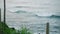 Waves crash against shoreline, viewed from tropical coast. Lush greenery frames seas surf, tranquil nature scene