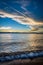 Waves crash softly on Lakeside Beach at Lake Tahoe with yellow and white clouds and a deep blue sky during sunset