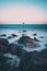 waves crashing over rocks at the seaside with a beach marker in the sea in the distance