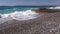 Waves crashing on pebbly shore with a pier