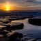 Waves crashing on rocks with pools water at sunset