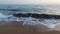 Waves lapping on a sandy kefalonia beach at sunset, with a warm glow on the horizon