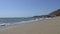 Waves of the pacific ocean beat on the shore in Malibu Beach Los Angeles California. The camera moves over the sand