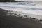 Waves rolling onto a black sand beach strewn with rocks and pebbles in Hana Bay, Maui