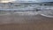 waves rolling onto a sandy beach against a blue sky with dramatic thunderclouds, sunset, beautiful landscape, slow motion