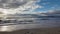 waves rolling onto a sandy beach against a blue sky with dramatic thunderclouds, sunset, beautiful landscape, slow motion