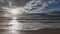 waves rolling onto a sandy beach against a blue sky with dramatic thunderclouds, sunset, beautiful landscape, slow motion