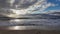 waves rolling onto a sandy beach against a blue sky with dramatic thunderclouds, sunset, beautiful landscape, slow motion