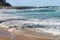 Waves rush onto shore over flat volcanic rocks with more rocks jutting out into the sea