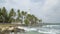 Waves rush to the rocky shore with a white lighthouse and palm trees