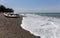 Waves with spray on the beach and a white rowboat on black sand.