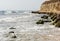 Waves, stones with green seaweed and a high steep shore on the B