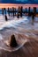 Waves swirl around pier pilings in the Delaware Bay at sunset, s