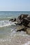 The waves of the turquoise sea break on the coastal boulders and a dense white foam is formed. Clear blue sky. White waves