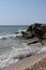 The waves of the turquoise sea break on the coastal boulders and a dense white foam is formed. Clear blue sky. White waves