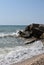 The waves of the turquoise sea break on the coastal boulders and a dense white foam is formed. Clear blue sky. White waves