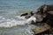 The waves of the turquoise sea break on the coastal boulders and a dense white foam is formed. Clear blue sky. White waves