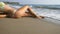 Waves washing over young female feet. Unrecognizable attractive woman in bikini lying on the sea beach. Tanned girl