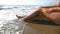 Waves washing over young female feet. Unrecognizable attractive woman in bikini lying on the sea beach. Tanned girl