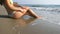 Waves washing over young female feet. Unrecognizable attractive woman in bikini lying on the sea beach. Tanned girl