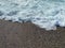 Waves of water in the sea and sand with small natural multi-colored stones on the seashore, small pebbles on the beach. Background