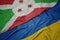 waving colorful flag of ukraine and national flag of burundi