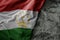 waving flag of tajikistan on the old khaki texture background. military concept