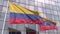 Waving flags of Colombia and Venezuela in front of a modern skyscraper facade