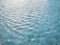 Waving pattern of vivid turquoise blue water in the swimming pool above stone tiles with soft light of reflection of the sunshine