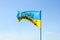 Waving Ukrainian yellow-blue flag against a blue sky. On the flag is the coat of arms of Ukraine and the inscription