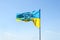 Waving Ukrainian yellow-blue flag against a blue sky. On the flag is the coat of arms of Ukraine and the inscription