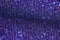 Wavy shimmering blue background. Texture with grain and purple sequins close-up