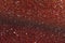 Wavy shimmering texture. Dark red background with graining and sequins close-up
