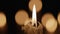 Wax burning candle flickers in dark on a black background with blurred candlelight bokeh effect. Background or