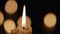 Wax burning candle flickers in dark on a black background with blurred candlelight bokeh effect. Background or