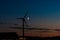 Waxing crescent moon passing behind a wind turbine at night