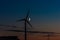 Waxing crescent moon passing behind a wind turbine at night