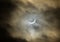 A waxing crescent shaped moon in an eclipse behind dark clouds a