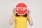 Way prohibited! Portrait of anonymous girl in yellow casual T-shirt covering face with stop symbol, holding red traffic sign,