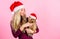 Ways to have merry christmas with pets. Girl attractive blonde hold dog pet pink background. Woman with puppy wear santa