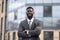 Wealthy african american entrepreneur young man standing outside modern office building, posing with folded arms