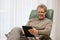 Wealthy mature man reading e-book while sitting in a chair in a bright living room