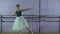 Wearing pointe shoes ballerina dances near barre in dancing hall