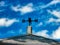 Weather vane on roof of a barn, with a defined sky in the background.