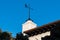 Weather vane on top of a white Spanish Colonial Architecture style building with a red tile roof