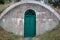 A weathered arched outdoor concrete underground cellar with green wooden door.